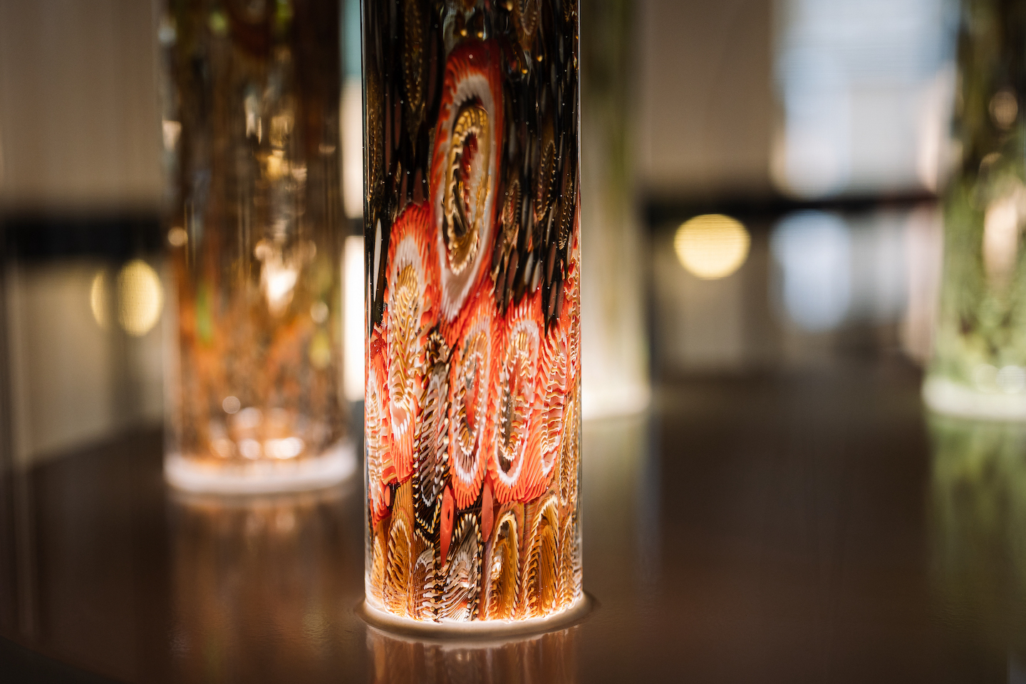 "Voice Cores #1-6" by Jenni Kemarre Martiniello A photograph of the Indigenous artwork installation "Voice Cores #1-6" by Jenni Kemarre Martiniello. The artwork comprises six colourful tall glass cores, lit from the base. Each core represents the shapes and resonances of the First Voices for each of the places named (#1 Rainforest, #2 Mutawintji, #3 Palawa, #4 Tarkayna, #5 Mungo, #6 Red Gibber Desert), its vowels consonants, syllables; each captured in the colours and forms of the natural environment of each place.